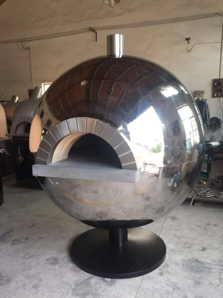Custom spherical stainless steel pizza oven with mirror-like reflective dome, stone-arched mouth, and black circular pedestal base