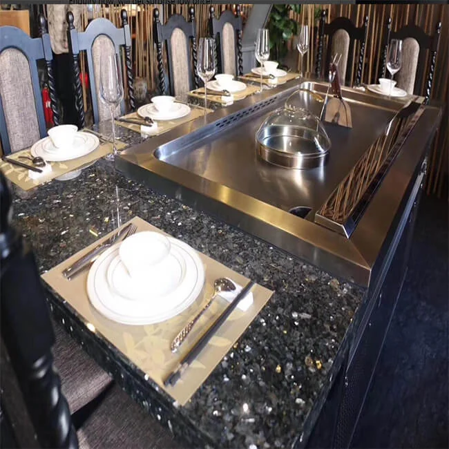 Luxury residential teppanyaki grill built into a dark stone dining table with cloche, plates, and stemware