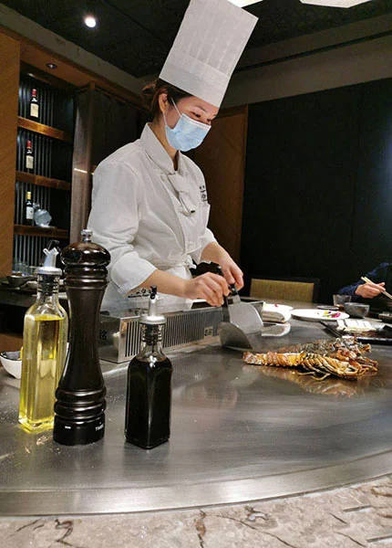 Female teppanyaki chef in toque preparing lobster on a teppan in a wine-lined private room