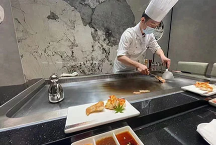 Chef cooking seafood on a commercial teppanyaki grill surface