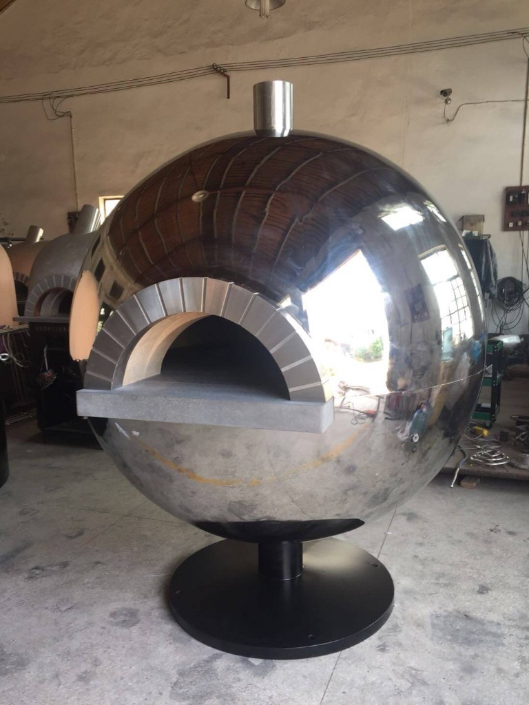 Custom spherical stainless steel pizza oven with mirror-like reflective dome, stone-arched mouth, and black circular pedestal base