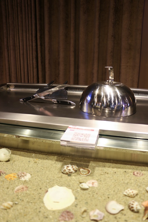 Vertical layers from pleated curtain to steel cooktop and illuminated sand-and-shell display at a hibachi station
