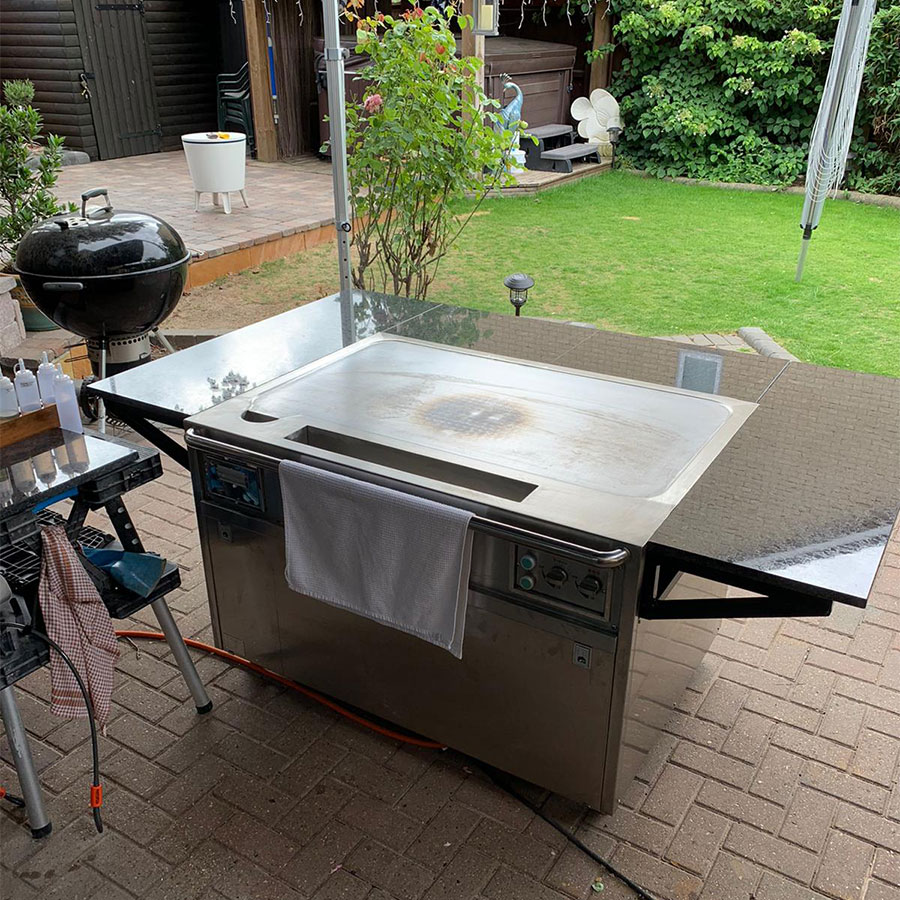 Outdoor stainless steel teppanyaki cooking station on a brick patio in a home garden