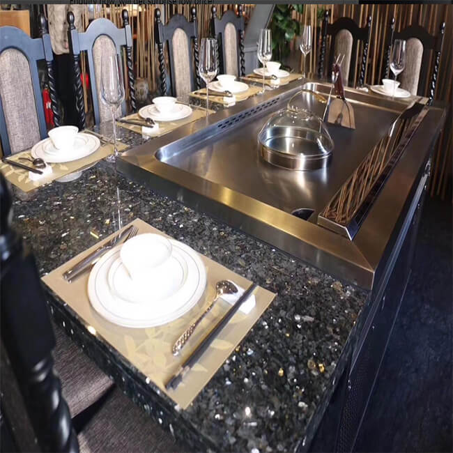 Luxury residential teppanyaki grill built into a dark stone dining table with cloche, plates, and stemware