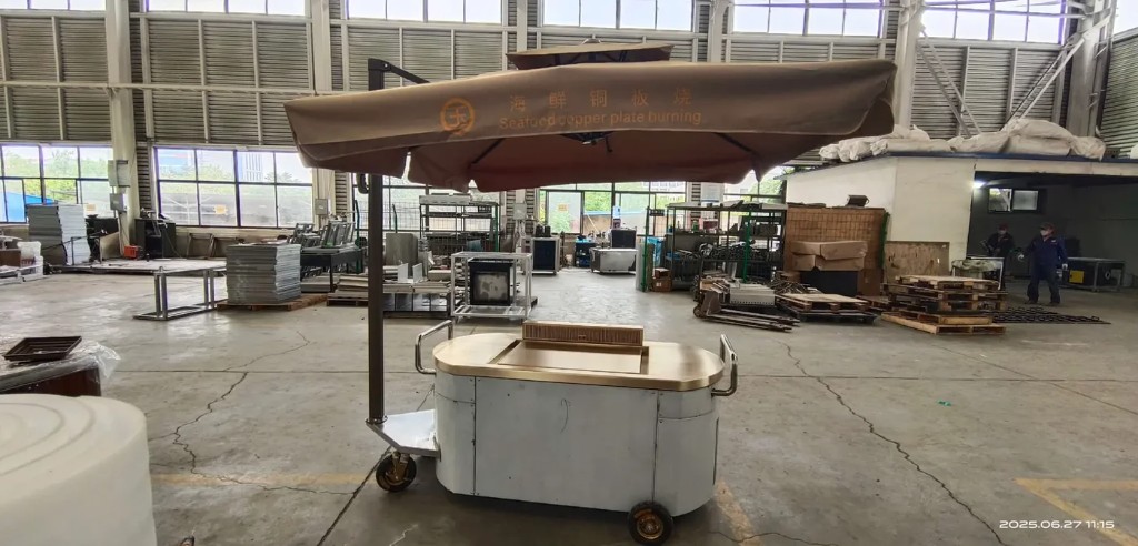 Mobile teppanyaki cart with umbrella shade over the cooktop.
