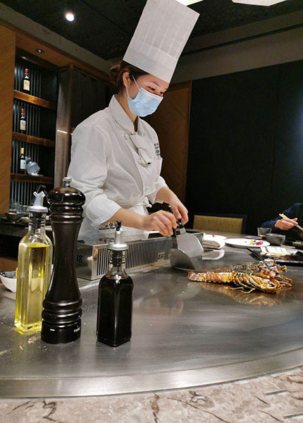 Female teppanyaki chef in toque preparing lobster on a teppan in a wine-lined private room
