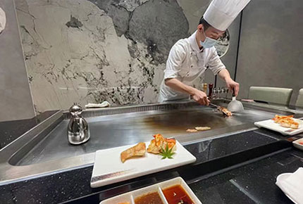 Chef cooking seafood on a commercial teppanyaki grill surface