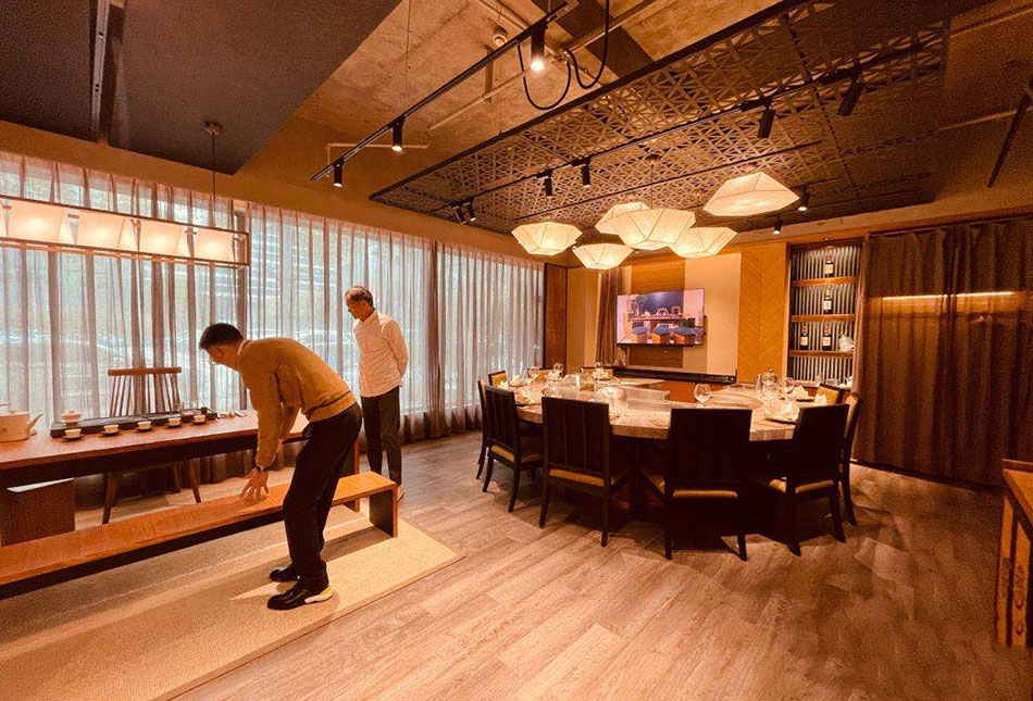 Tea tasting area with long wooden tea table, porcelain tea set, and marble dining table beyond