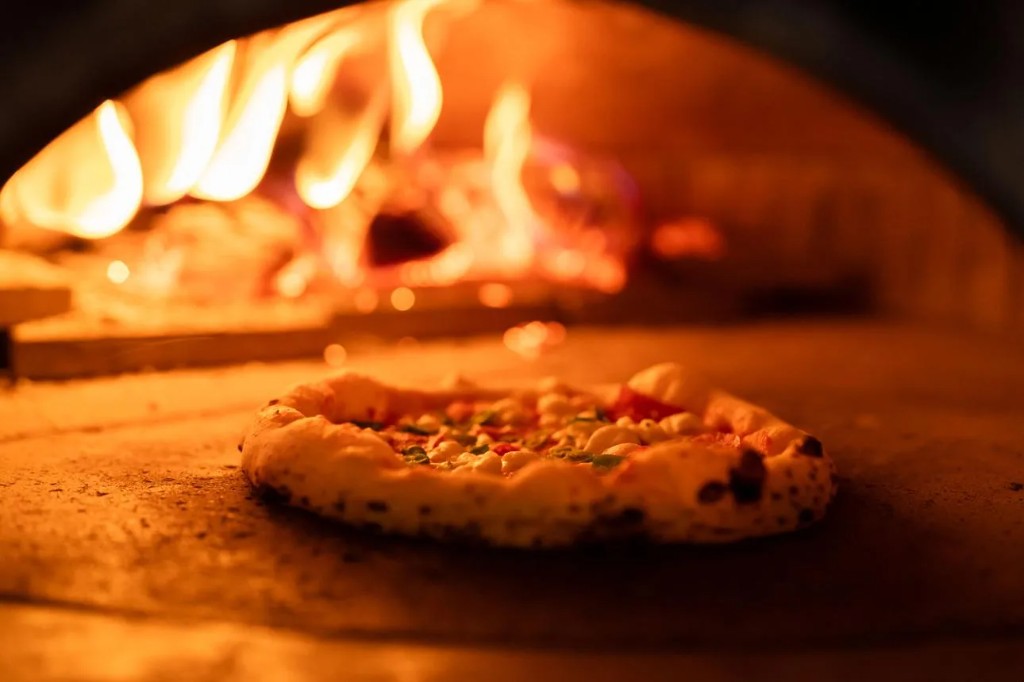 Commercial wood fired and gas powered pizza oven with lava stone deck in a restaurant kitchen